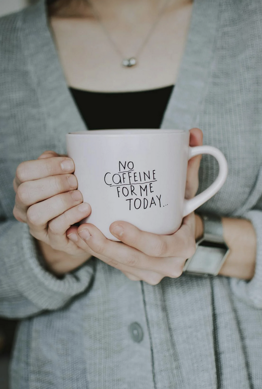 A lady holding a coffee cup saying no caffeine for me today